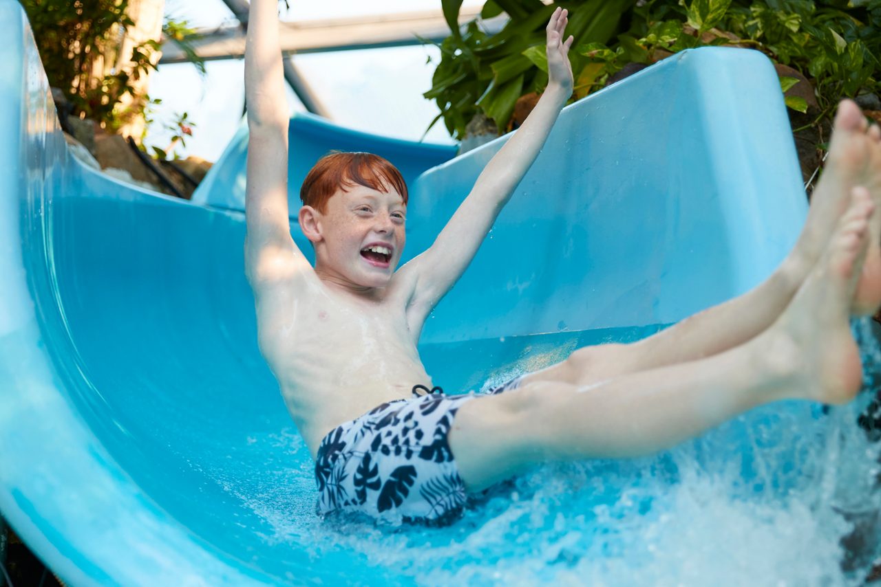 Young boy with his arms in the air as he splashes down a flume.
